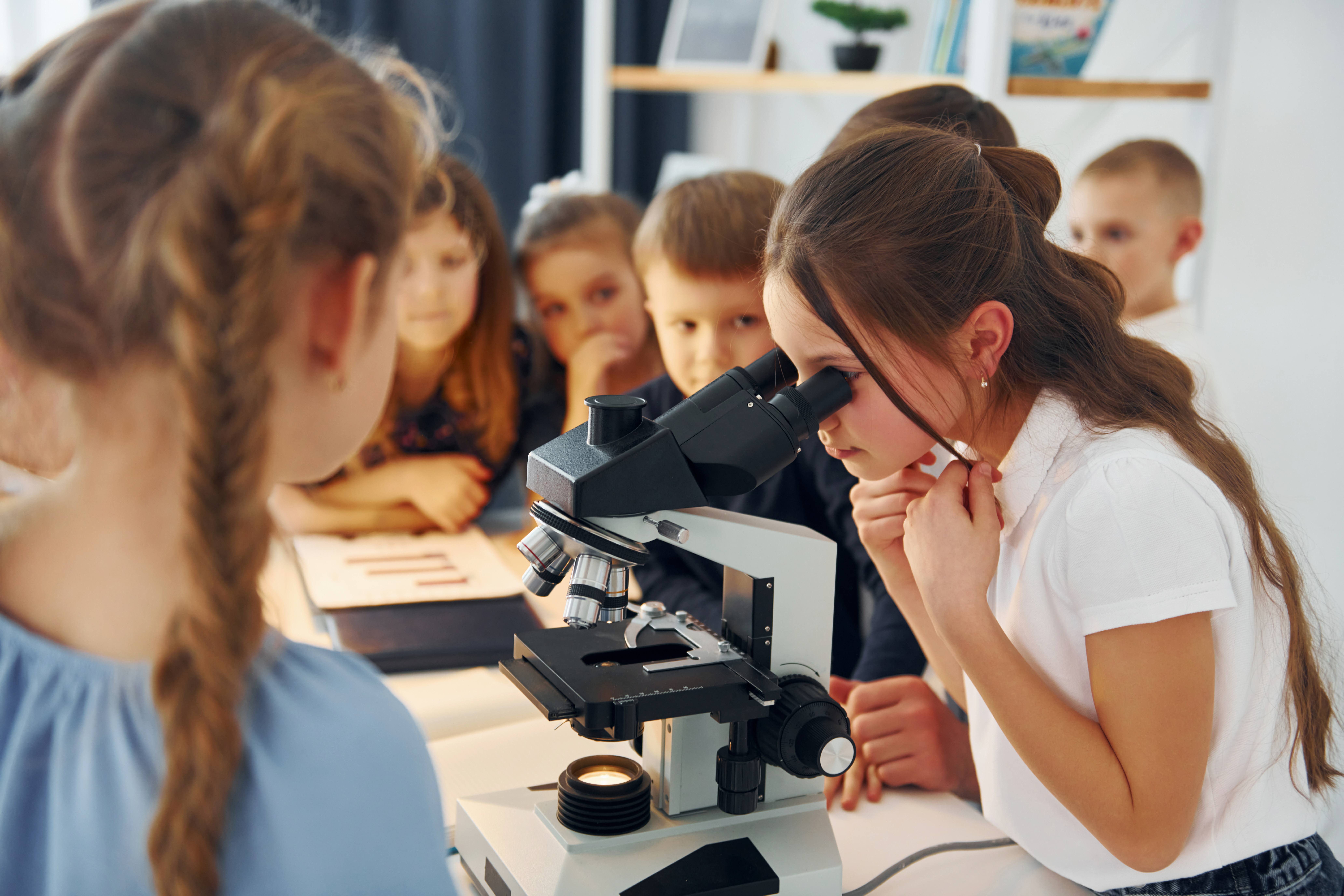 Zdjęcie przedstawiające grupę dzieci. Jedno z nich spogląda przez mikroskop.